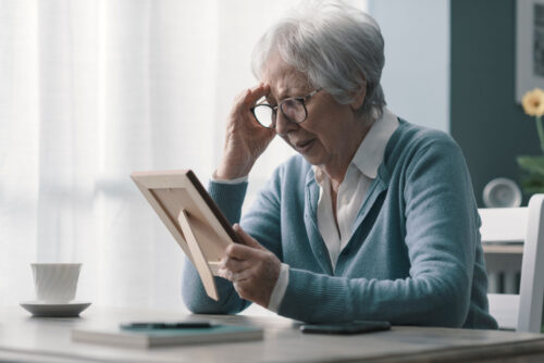 Sad woman at home grieving the loss of her husband, she is holding a picture and crying